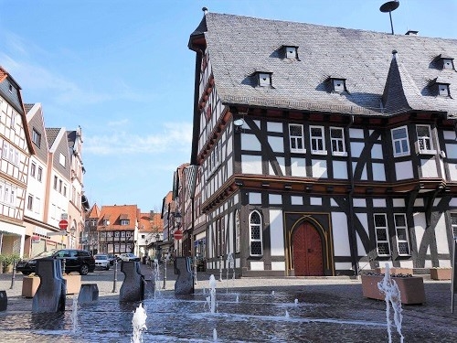 Historische Fachwerkhäuser an einem gepflasterten Platz mit Wasserspielen in der Stadt Schotten.