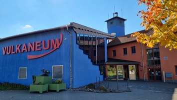 Das Vulkaneum in Schotten mit blauem Hauptgebäude, roter Aufschrift 'VULKANEUM' und angrenzendem orangefarbenem Gebäudeteil mit Turm.