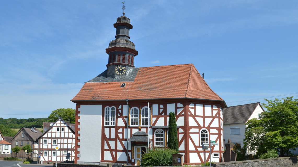 Evangelische Fachwerkkirche mit rotem Ziegeldach und Uhrturm vor blauem Himmel in Eichelsachsen.
