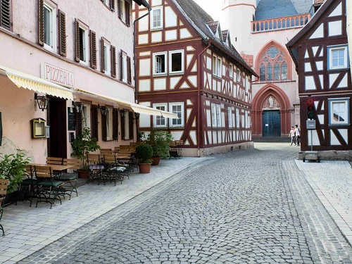 Kopfsteinpflasterstraße in Schotten mit Fachwerkhäusern, einem Pizzeria-Schild und einer Kirche im Hintergrund.