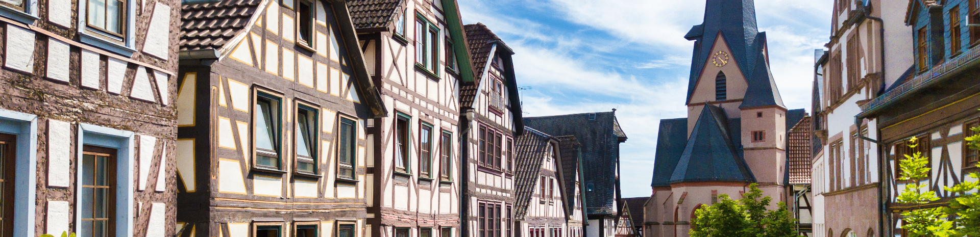 Blick auf die historische Altstadt von Schotten mit Fachwerkhäusern und einem Kirchturm im Hintergrund unter blauem Himmel.
